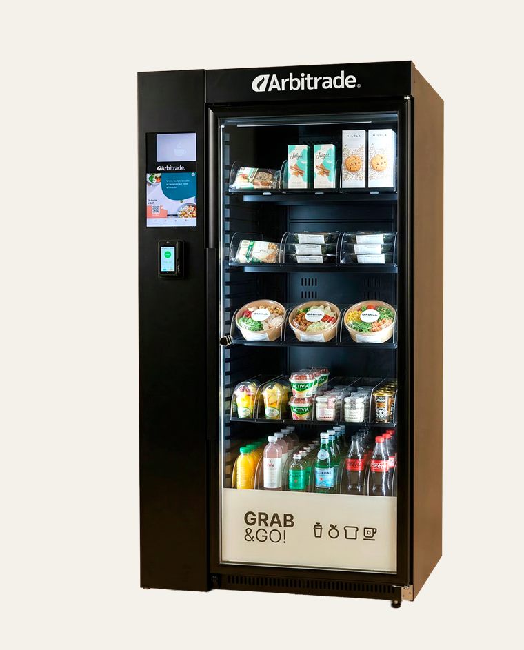 Una SmartShop vista de frente, con la puerta acristalada, la pantalla táctil, el lector de tarjeta y cinco baldas llenas de comida y bebida.